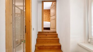 Un escalier en bois mène à une chambre à coucher qui contient un lit, une fenêtre et une porte.