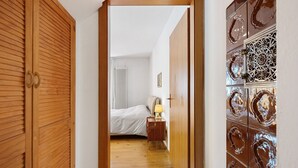 Un couloir mène à une chambre à coucher qui contient un lit, une table de chevet et une lampe.