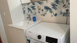 Kompakti pyykinpesutila, jossa on pesukone, pesuallas ja sininen kuppi.