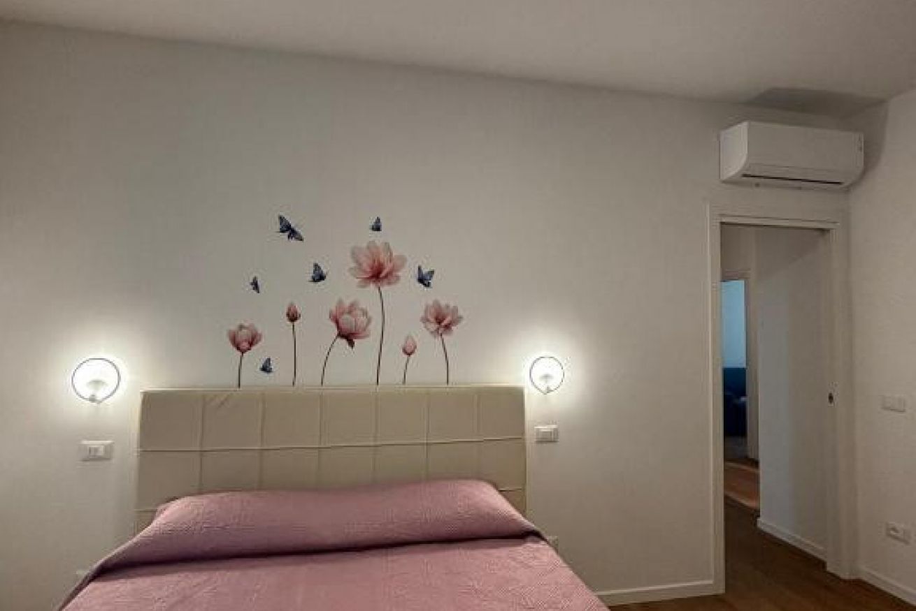A bedroom with a bed, a wall-mounted air conditioner, and a door leading to another room.
