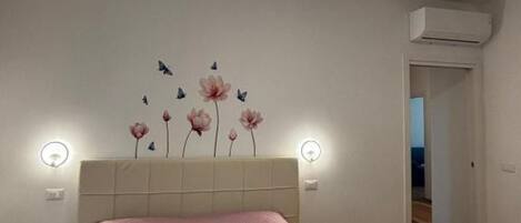 A bedroom with a bed, a wall-mounted air conditioner, and a door leading to another room.