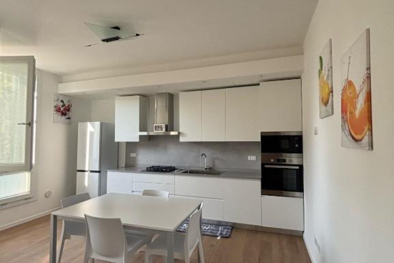 A modern kitchen with white cabinets, a dining table, and a large window.