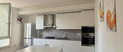 Una cocina moderna con armarios blancos, una mesa de comedor y un ventanal grande.