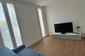 A modern living room with a flat-screen TV on a white console, large windows, and a blue sofa. - The Space✨ Brand New, Modern & Super Comfortable Home at the Gates of Venice – All the Best, Without the Stress ✨Welcome to your brand-new “home away from home”!This property has been completely renovated from top to bottom: from shiny new floo (Venice)