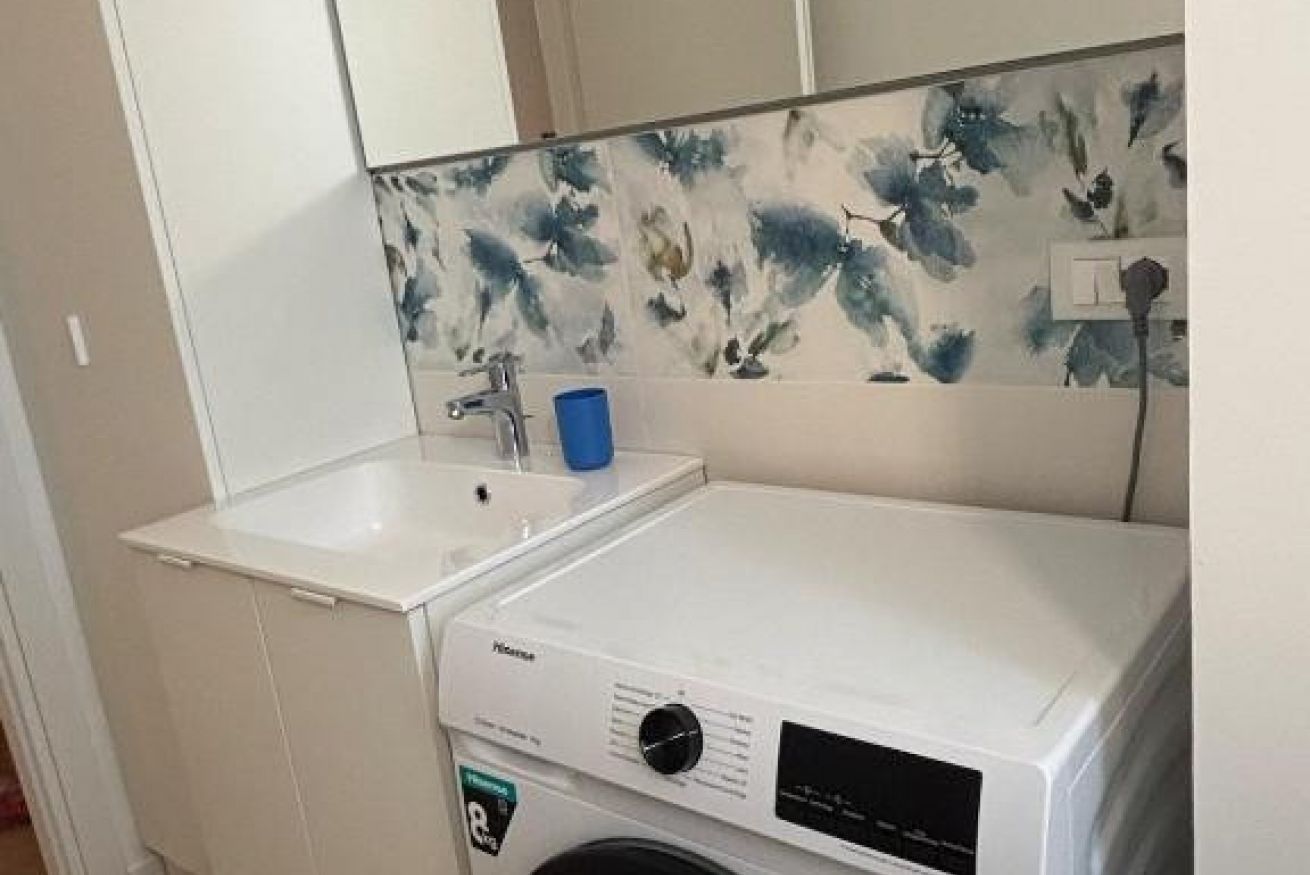 A compact laundry area with a washing machine, a sink, and a blue cup.
