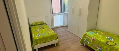 A small bedroom with two single beds, a wardrobe, and a window.