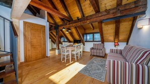 Een ruime loft met zichtbare houten balken, een eethoek, een gestreepte bank en een trap.