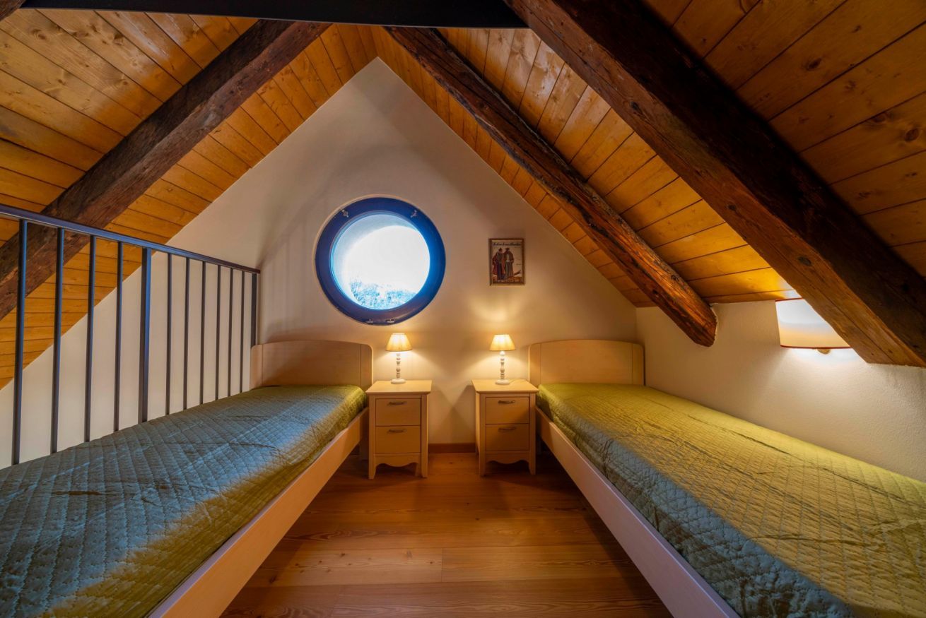 A small attic bedroom with two single beds, a skylight, wooden beams, and a staircase.