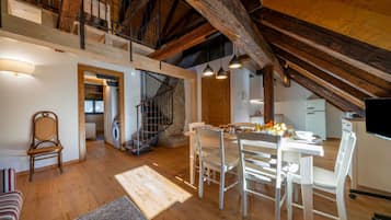 Spazioso loft con soffitto alto, travi a vista in legno, angolo pranzo con tavolo e sedie, cucina e una scala che conduce a un piano superiore.