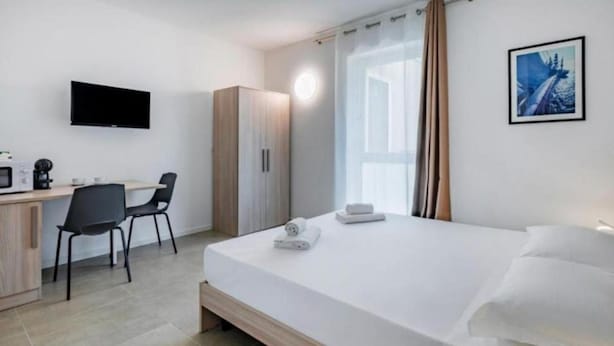 A modern hotel room with a bed, a desk, a chair, a wardrobe, a flat-screen TV, and a window with curtains. - 🏡 Modern & Functional Rooms in Mestre – Brand-New Guesthouse with Free ParkingPerfectly located for Venice: bus no. 5 passes every 10 minutes and takes you directly to the historic center in just a few minutes! Rooms are equipped with a comfortable  (Venice)