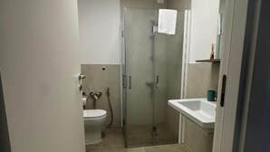 Un baño pequeño con inodoro, cabina de ducha de cristal y lavamanos.