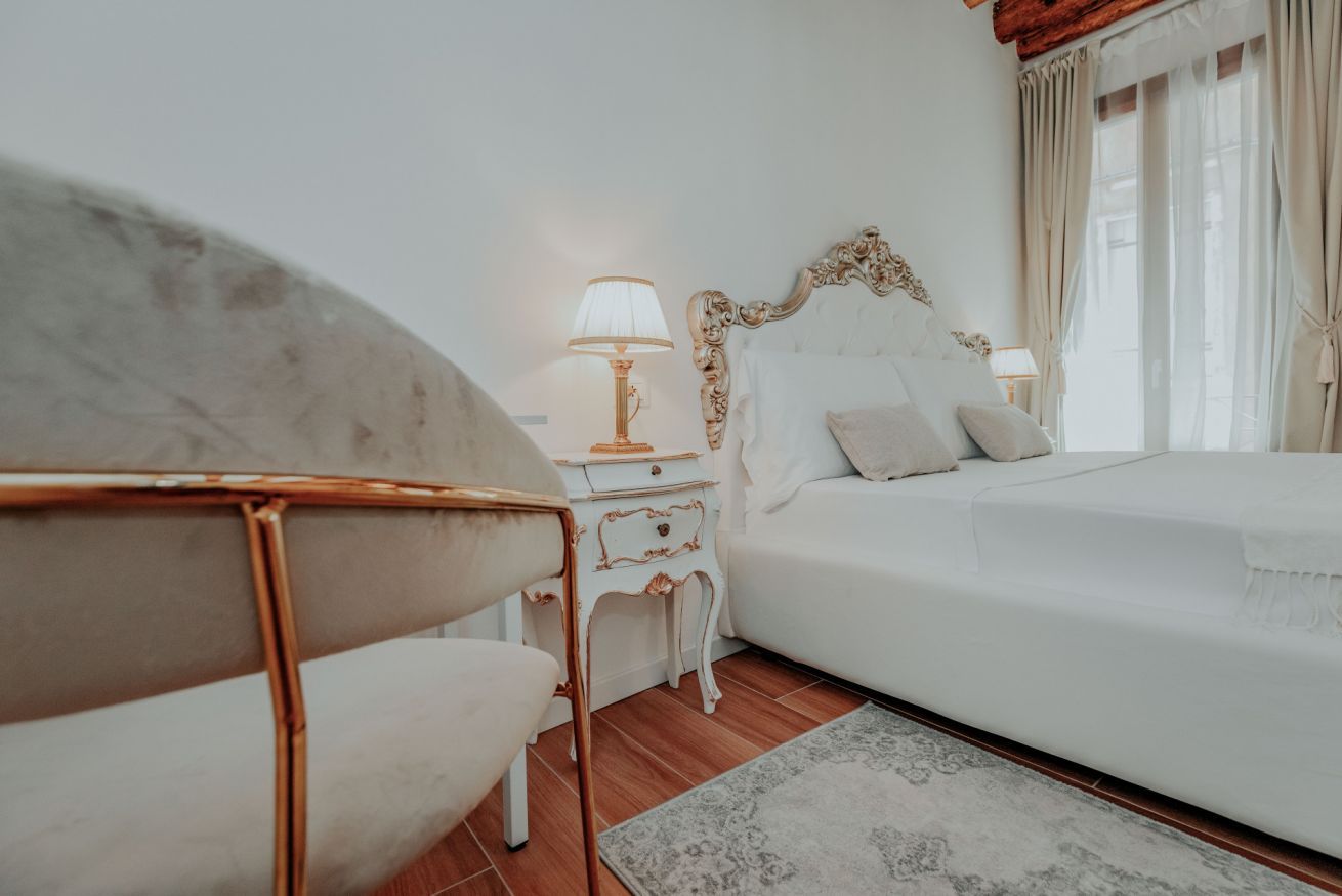 A bedroom with a bed, nightstand, lamp, chair, and a window with curtains.