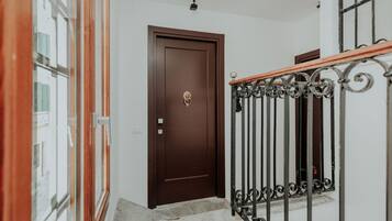 Una escalera con barandilla de madera y balaustradas de metal que conduce a una puerta marrón con aldaba dorada.