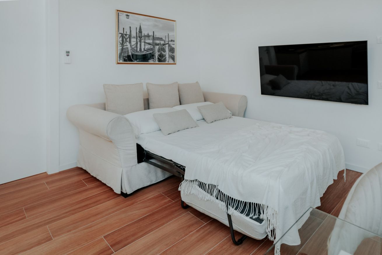 Um quarto com uma cama, um sofá, uma televisão e um quadro na parede.