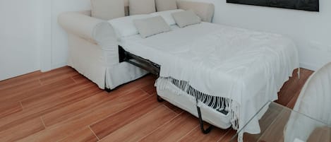 Um quarto com uma cama, um sofá, uma televisão e um quadro na parede.