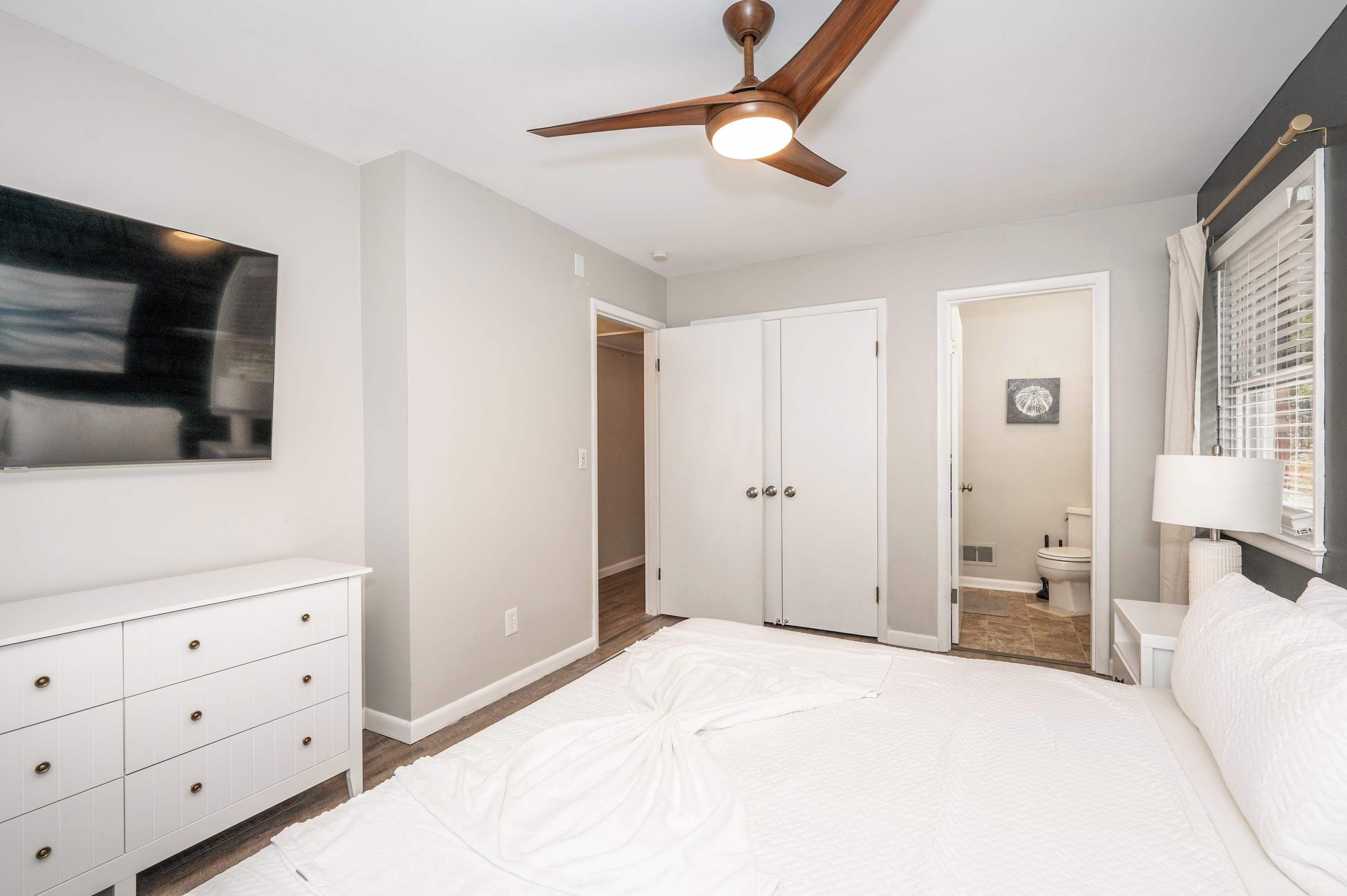 A bedroom with a bed, a ceiling fan, a white dresser, and a door leading to a bathroom.