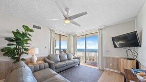 Ein modernes Wohnzimmer mit einer grauen Ledersofa, einem Deckenventilator, einem Fernseher und Meerblick durch große Fenster.