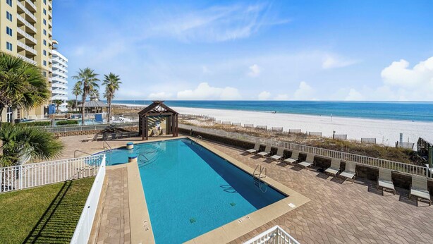 Ein Pool mit Blick auf den Strand, umgeben von Liegestühlen und Palmen.