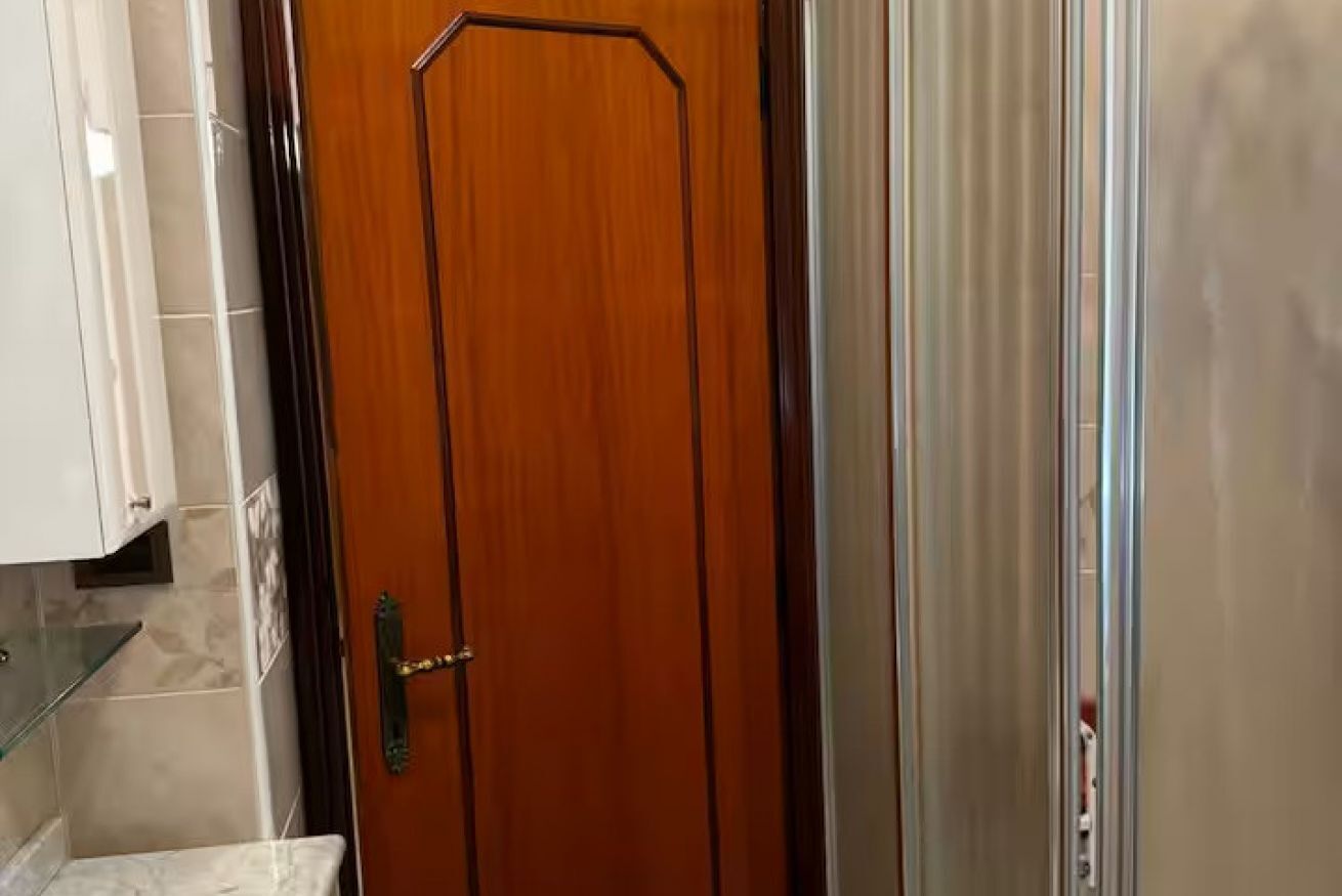 Uma porta de madeira com maçaneta de latão, uma prateleira de vidro e parede revestida de azulejos.