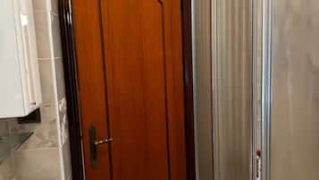 Uma porta de madeira com maçaneta de latão, uma prateleira de vidro e parede revestida de azulejos.