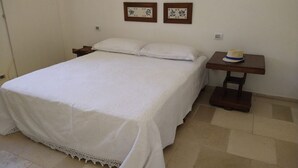 A bedroom with a bed, a nightstand, a small table with a hat, and four framed pictures on the wall. - The Space🌿 Trullo Scirocco – Sleep Under Puglia’s Stars, Live the Magic of the Trulli ✨Wake up to birdsong, breathe in the scent of centuries-old olive trees, and walk barefoot on warm stone. Welcome to Trullo Scirocco, a one-of-a-kind home in t (Ostuni)