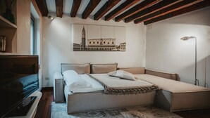 Quarto com cama, mesas de cabeceira, televisão, tapete estampado e quadro de um edifício na parede.