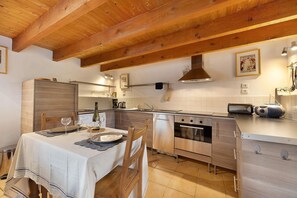 A modern kitchen with wooden beams, stainless steel appliances, and a dining area with a table set for two. - Gîte des Fraignaies with Private Pool and Terrace in Saint-Juire-Champgillon (Saint-Juire-Champgillon)