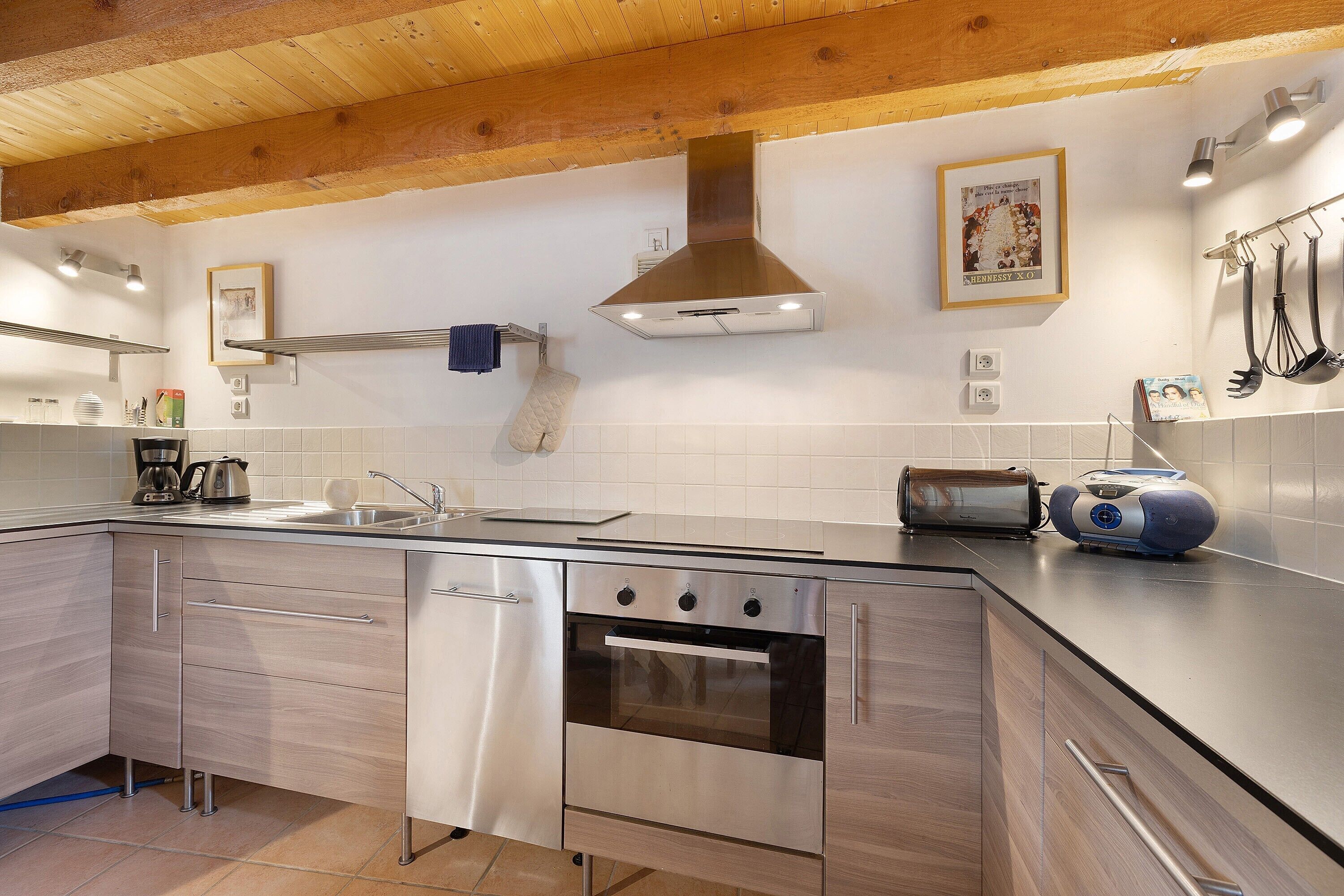 A modern kitchen with stainless steel appliances, wooden ceiling beams, and a tiled backsplash.