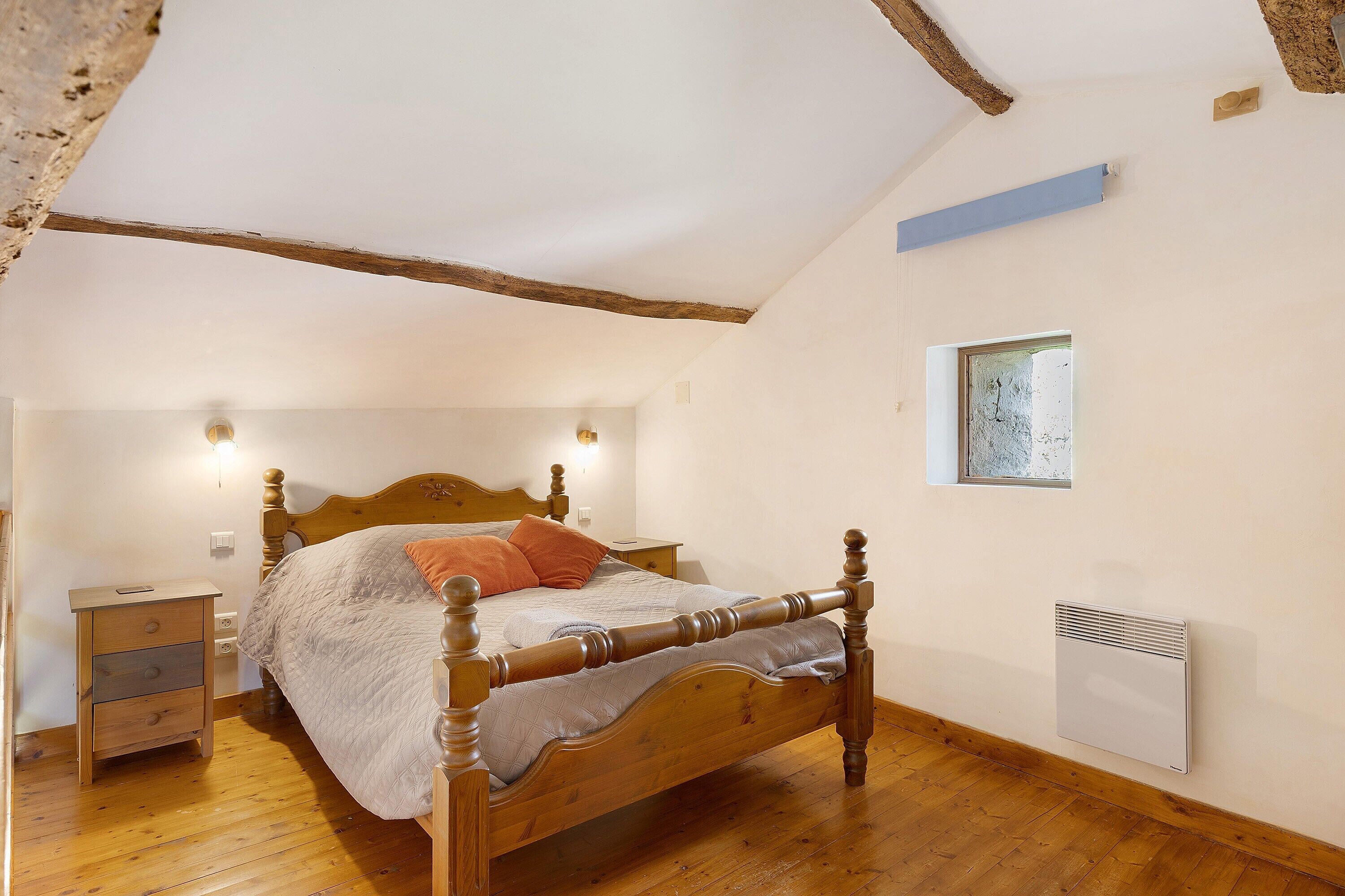 Ein Schlafzimmer mit einem Holzbett, einem Nachttisch, einer Wandheizung und einem Fenster.