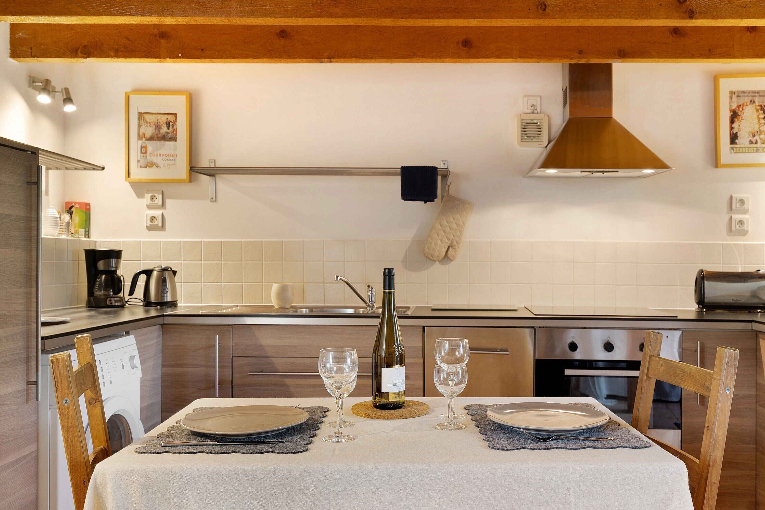 A kitchen with wooden cabinets, a stainless steel range hood, a wine bottle, and two glasses on a table.