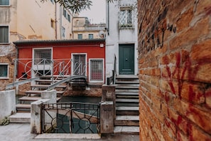 A narrow alleyway with a red building, a green door, and a metal staircase leading to a bridge over a canal. - The SpaceWelcome to the heart of Venice, just a few steps from the magnificent Basilica dei Frari!This apartment is perfect for couples, solo travelers or small families who wish to immerse themselves in the authentic atmosphere of the city without givin (Venezia)