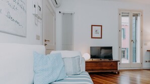 Un dormitorio con cama, televisor, radiador y puerta que da a un balcón.