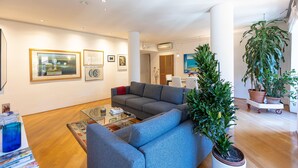 A modern living room with a grey sofa, a glass coffee table, and a large potted plant. - Rental in Rome San Gioacchino View Apartment (Rome)