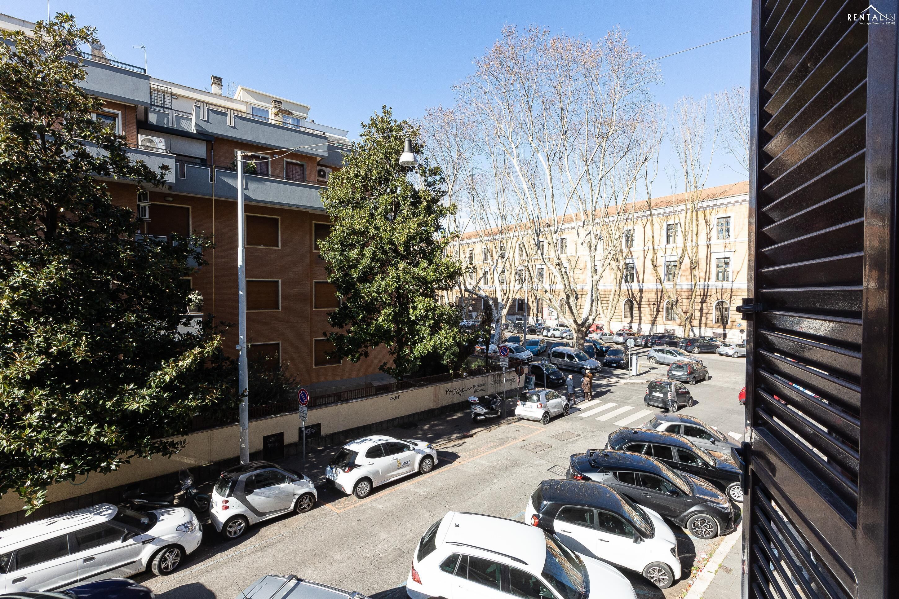 A street view with parked cars, a tree, and a building with multiple windows.