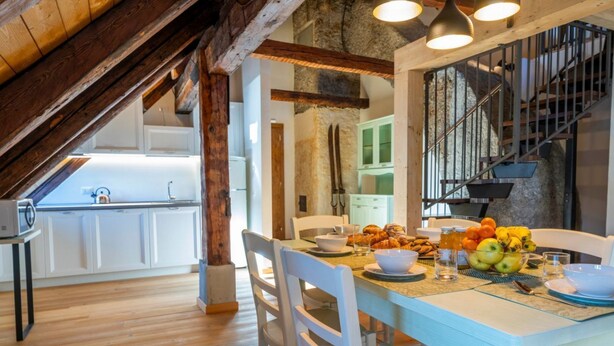 Een eetruimte met een tafel gedekt voor twee personen, een keuken op de achtergrond en een trap naar een hoger gelegen verdieping.