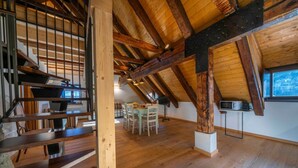 Een ruime loft met zichtbare houten balken, een eethoek en een trap.