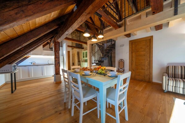 Un comedor con mesa y sillas de madera, una escalera y una cocina al fondo.