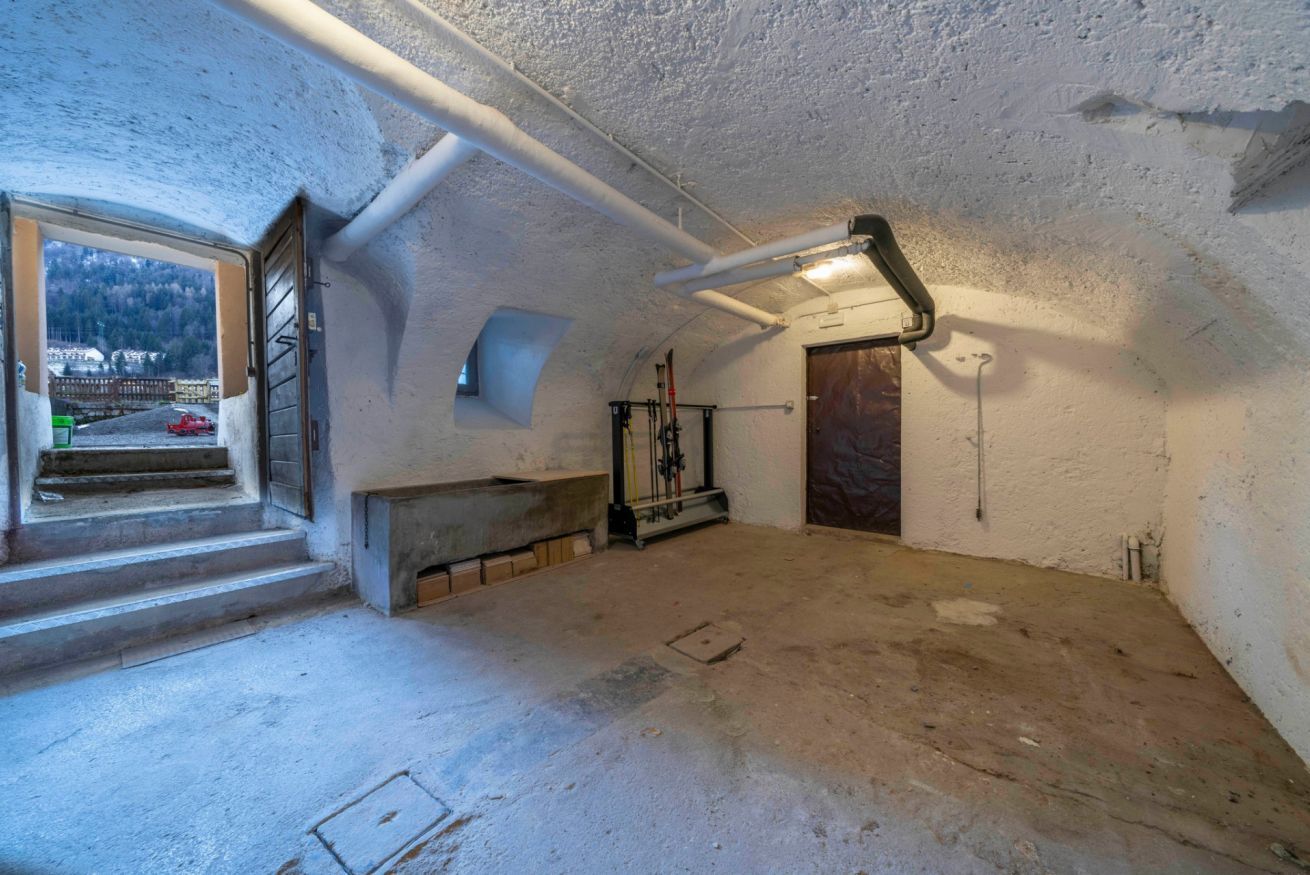 An attic room with a concrete floor, a window with a view of a road and buildings, a door, and a metal staircase.
