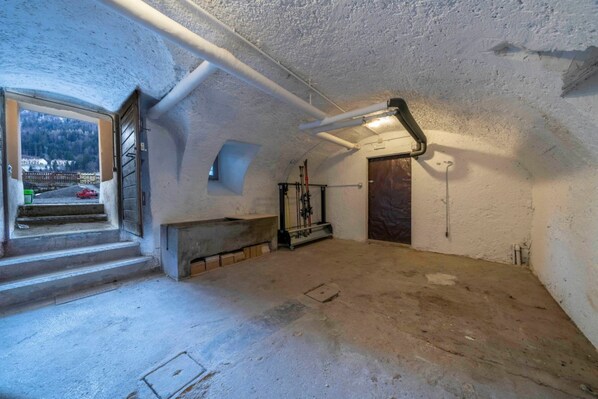 An attic room with a concrete floor, a window with a view of a road and buildings, a door, and a metal staircase.