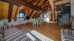 Een ruime loft met zichtbare houten balken, een eethoek, een trap en een gezellige zithoek.