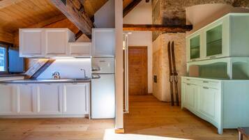 Cucina con mobili bianchi, un frigorifero e soffitto in legno.