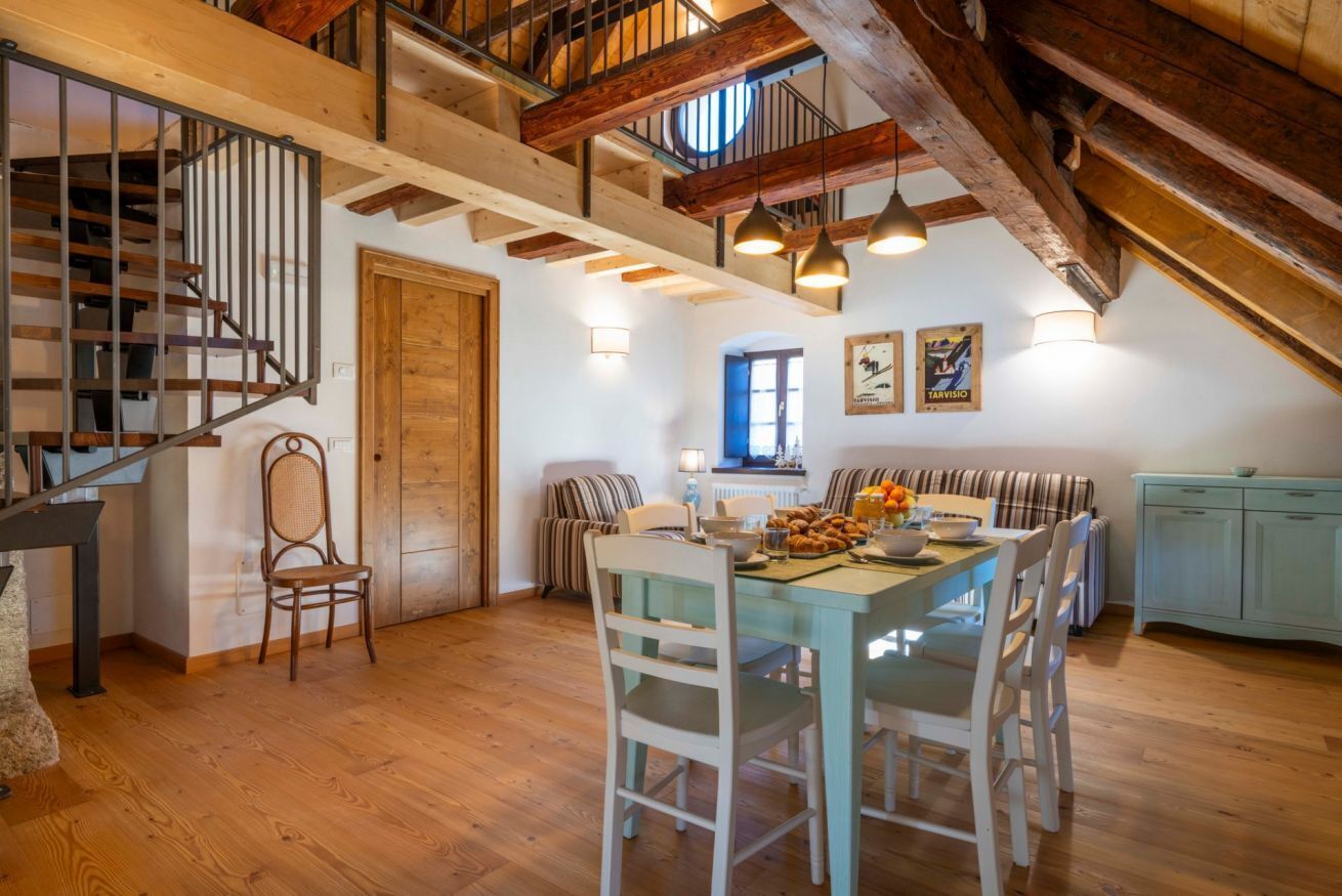 Un espace repas comprenant une table en bois, des chaises et un escalier doté d’une rampe en métal.