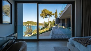 Un dormitorio moderno con un amplio ventanal corredera que da a un balcón con vistas panorámicas a un lago y árboles.