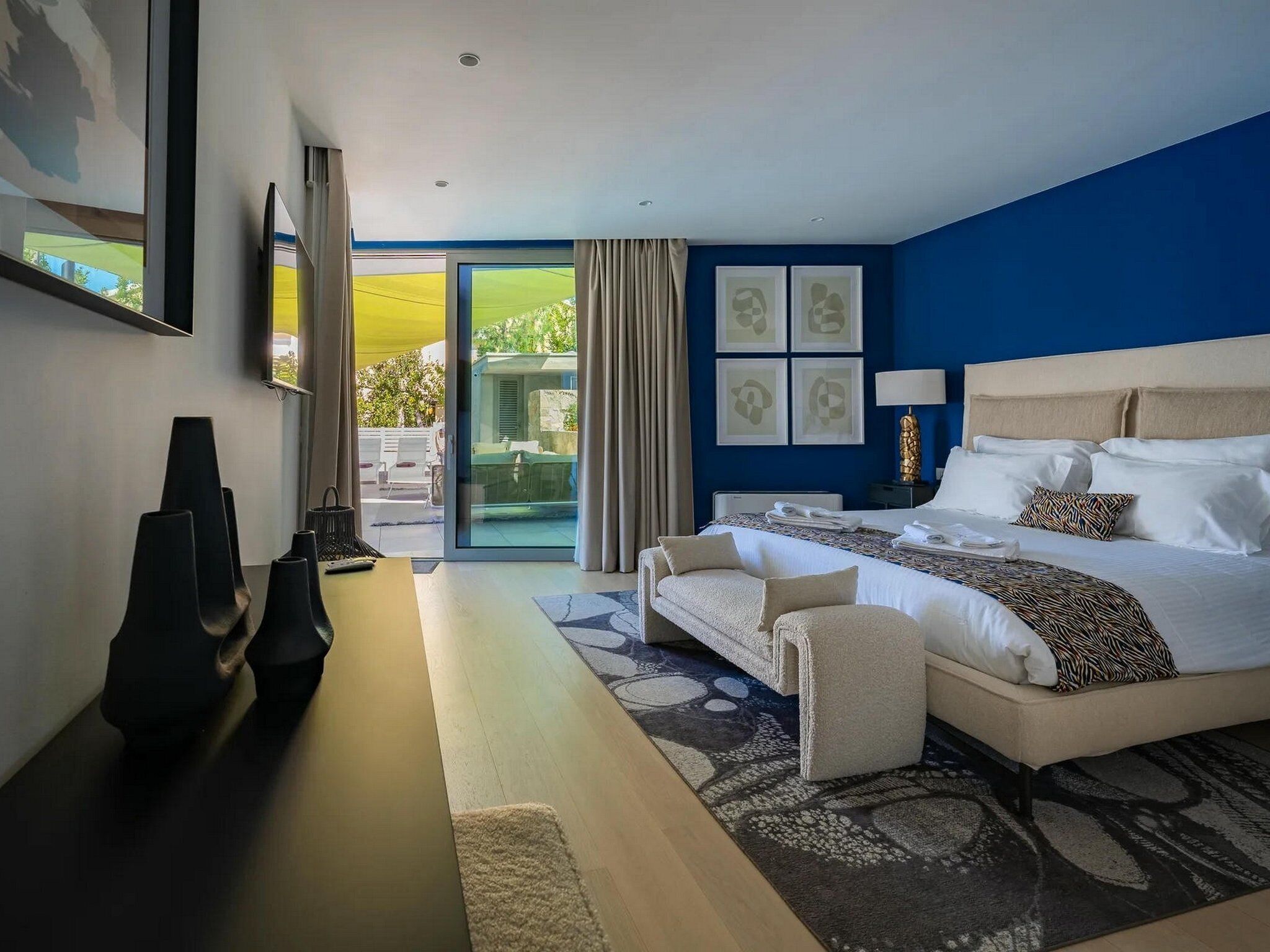 A modern hotel room with a large bed, a desk, and a view of a green landscape through the glass door.
