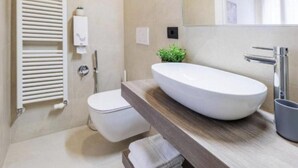 Une salle de bain moderne avec des toilettes blanches, un grand lavabo ovale et un meuble-lavabo en bois.