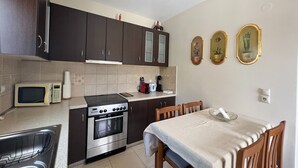 A compact kitchen with dark cabinets, a microwave, a stove, and a dining area with a table and chairs. - Kika Residence - 2 Bedroom House With Barbeque (Kefalonia)