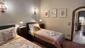 Habitación de hotel con dos camas, una mesita de noche, apliques de pared y cuadros en la pared.