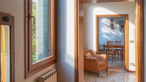 Una habitación con puerta de madera, ventana, radiador, una silla y una mesa con sillas.