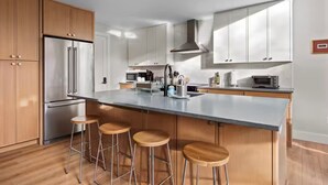 Uma cozinha moderna com uma ilha grande, eletrodomésticos de aço inoxidável, armários de madeira e banquetas de bar.