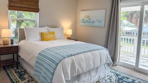 A bedroom with a bed, two bedside lamps, a window with a view, a ceiling fan, and a large window with curtains. - 8th At The Bay, New Listing (Port St. Joe)